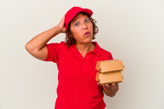 Middle age delivery woman taking burguers isolated on white background being shocked, she has remembered important meeting.