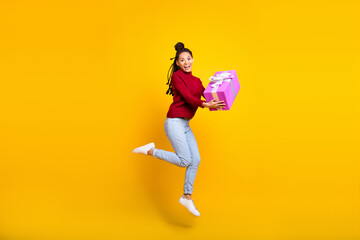 Fototapeta na wymiar Full length high of shiny adorable dark skin woman dressed red sweater jumping holding gift box isolated yellow color background