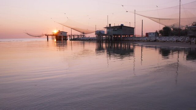 Landscape shot of fishing huts on river at sunrise with typical italian fishing machine, called "trabucco",Lido di Dante, fiumi uniti Ravenna near Comacchio valley.