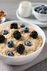 Tasty oatmeal porridge with blackberries and blueberries in bowl on table