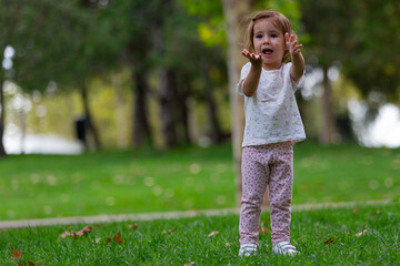 Fototapeta premium Small girl standing with outstretched hands on the grass in the park. Kids outdoors