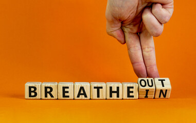 Breathe in and out symbol. Doctor turns cubes, changes words breathe in to breathe out. Beautiful orange background, copy space. Medical, lifestyle and breathe in and out concept.