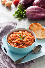 Eggplant caviar in blue bowl and fresh vegetables on background