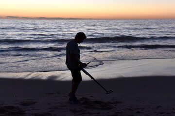 Fototapeta na wymiar silhouette of a person using a metal detector on a beach