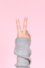 Female hand in gray knitted sweater with beautiful manicure - pink nude nails making victory sign...