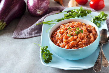 Eggplant caviar in blue bowl and fresh vegetables on background