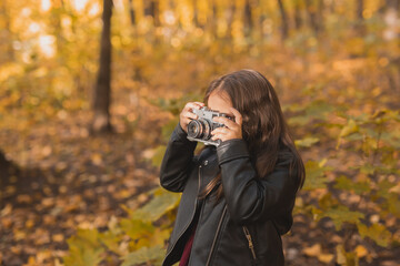 Child girl using an old-fashioned camera in autumn nature. Photographer, fall season and leisure concept.