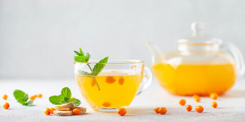 Hot autumn tea with sea buckthorn, ginger and mint in a glass teapot on a gray background