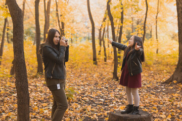 Fototapeta premium Mother photographer takes pictures of a her daughter in the park in autumn. Hobbies, photo art and leisure concept.