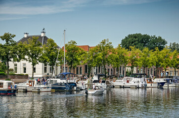 Fototapeta na wymiar Blokzijl, The Netherlands, August 12, 2021: small yachts and sailboats moored at the old town's harbour, lined with trees and historic brick houses