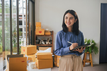 Plakat Portrait business Asian woman smile and use tablet checking information on parcel shipping box before send to customer. Entrepreneur small business working at home. SME business online marketing.