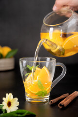 Glass cup with fruit herbal tea on black background. Calendula healthy tea