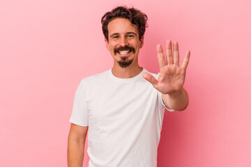 Young caucasian man isolated on pink background smiling cheerful showing number five with fingers.