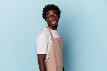 Young african american store clerk isolated on blue background looks aside smiling, cheerful and pleasant.
