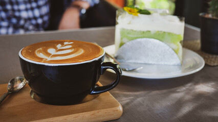 Hot cappuccino coffee in a white cup Served on a wooden tray And there is a spoon on the side Cafe atmosphere Blur the cake and people 