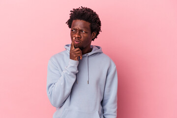 Young african american man isolated on pink background looking sideways with doubtful and skeptical expression.