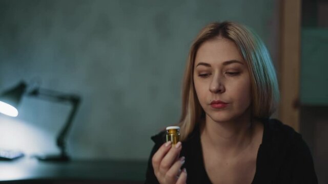 Thoughtful woman turns glass drug bottle with unregistered nutritional products doubting in doctor prescription in semi-dark room closeup slow motion