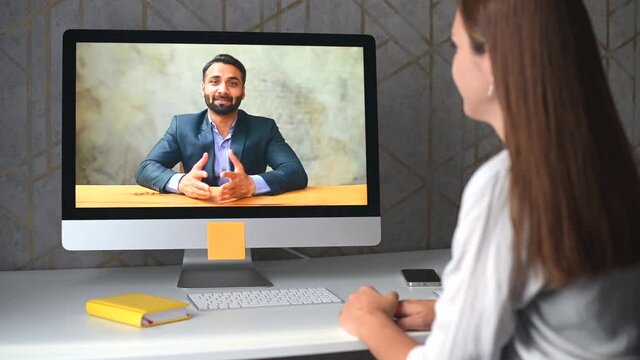 Young woman talking online with Indian male colleague or friend via video connection on the laptop. Female student listening educational course from ethnic tutor. Video call, virtual meeting