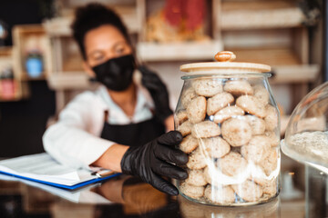 African American middle aged female worker with protective mask on face working in bakery. Coronavirus, Covid-19 concept.