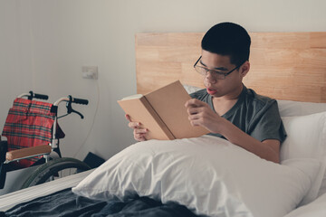 Smart handicapped teenager boy on the bed reading and learning online with happy face, Lifestyle of...