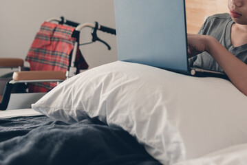 Asian handicapped teenager boy using computer and listening music video in the morning on bed and...