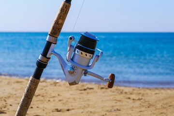 Fishing rod with spinning reel on beach. Saltwater fishing on sea shore. Copy space.