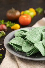 Green potato chips with herbs and tomatoes on black concrete background. Side view, close up,...