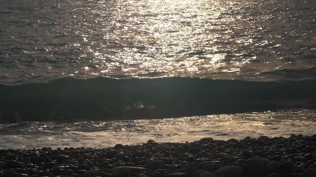 Tropical beach. Small waves breaking gently on a pebble shore at sunset.
