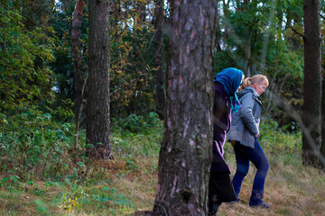 Defocus side view among trunk of two woman walking in pine forest. Mushroom picking season, leisure and people concept, mother and daughter walking in fall forest. People lost. Out of focus