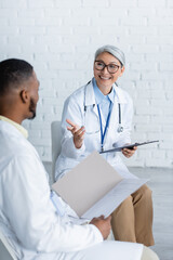 happy asian doctor pointing with hand while talking to blurred african american colleague