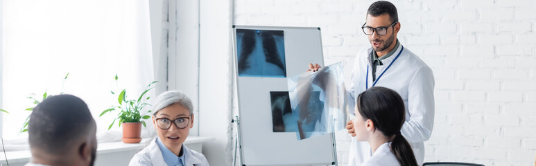 young doctor showing lungs x-rays to multiethnic colleagues, banner