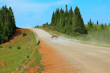 A car climbs a dirt road up a hill in clouds of dust