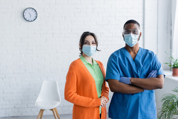 african american doctor and young woman in medical masks looking at camera in vaccination center