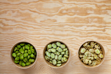 Raw broad beans in bowls. Peeled, unpeeled and separated seed skins of broad beans top view with copy space. - obrazy, fototapety, plakaty