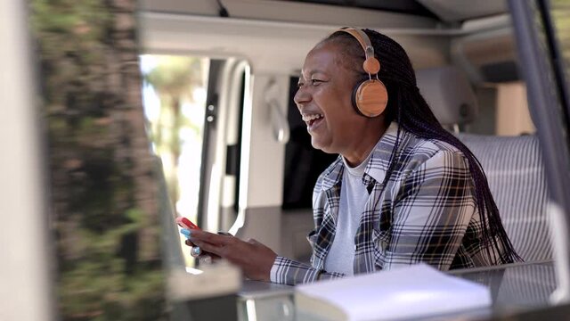 African senior woman using smartphone inside mini van camper - Elderly person enjoy technology on road trip vacation