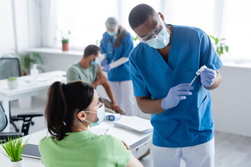 african american doctor preparing vaccine near woman in medical mask and blurred colleague with...