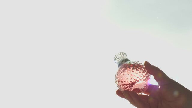 pink crystal bottle spray with perfume in hand on the background of the window and sunlight, hard shadows, sunbeam and glare