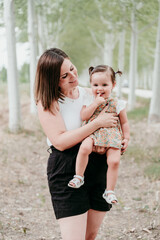 portrait of beautiful mother holding baby girl in trees path. Family, fun and nature concept