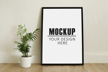 Frame, poster mock up with vertical black frame and plant. Empty frame standing on the wooden...