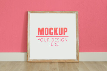 Obraz premium Frame, poster mock up with wooden frame. Empty frame standing on the wooden floor, pink wall. Free space for your picture or text, copy space. Minimalist design.