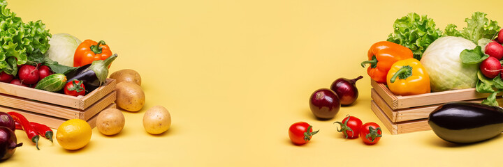 A set of fresh vegetables on a yellow background in wooden boxes. Potatoes,tomatoes, radishes,onions,cucumbers, eggplant, cabbage, pepper, lemon. Copy space.
