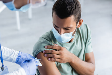 blurred nurse giving injection of vaccine to young man in protective mask