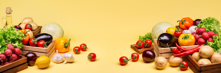 Autumn harvest of vegetables on a yellow background. Tomatoes, potatoes, radishes, lettuce, cabbage, lemons, eggplant, garlic, vegetable oil in wooden boxes. Horizontal  banner. Perfect retouching.
