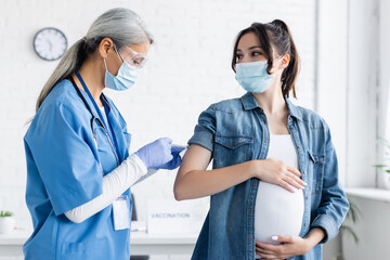 middle aged asian woman in medical mask and latex gloves vaccinating pregnant woman - Powered by Adobe