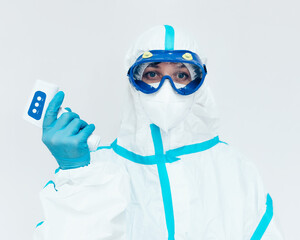 A medic in a protective medical suit and mask holds a modern infrared thermometer in his hand....