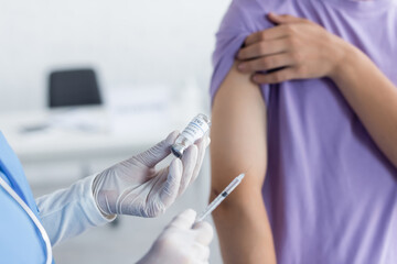 cropped view of physician holding jar and syringe with vaccine near blurred patient