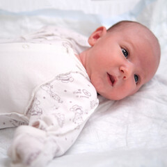 Portrait of a baby boy aged one month lying with his eyes open in a crib. Caucasian child in the children bedroom on the bed