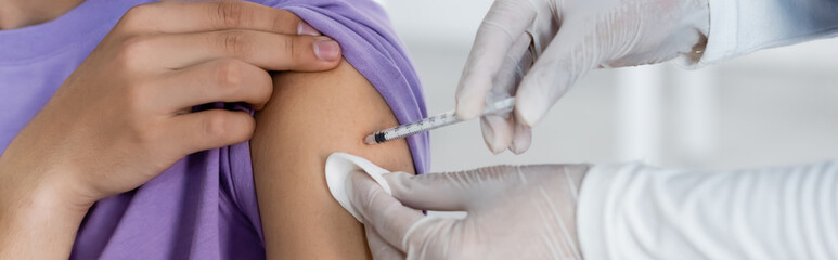 partial view of doctor in latex gloves vaccinating young man, banner