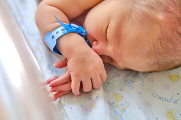 A newborn baby with a maternity hospital bracelet on his arm is sleeping in a crib. A newly born...