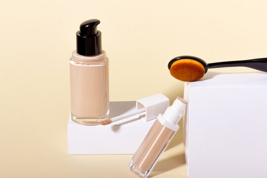 Liquid foundation in a bottle on a stand, makeup brush and concealer. Face corrector on beige background with copy space. Packaging mockup with copy space